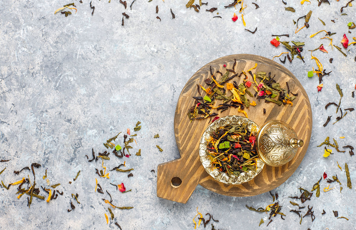 Assorted loose leaf teas in a brass bowl on a wooden board